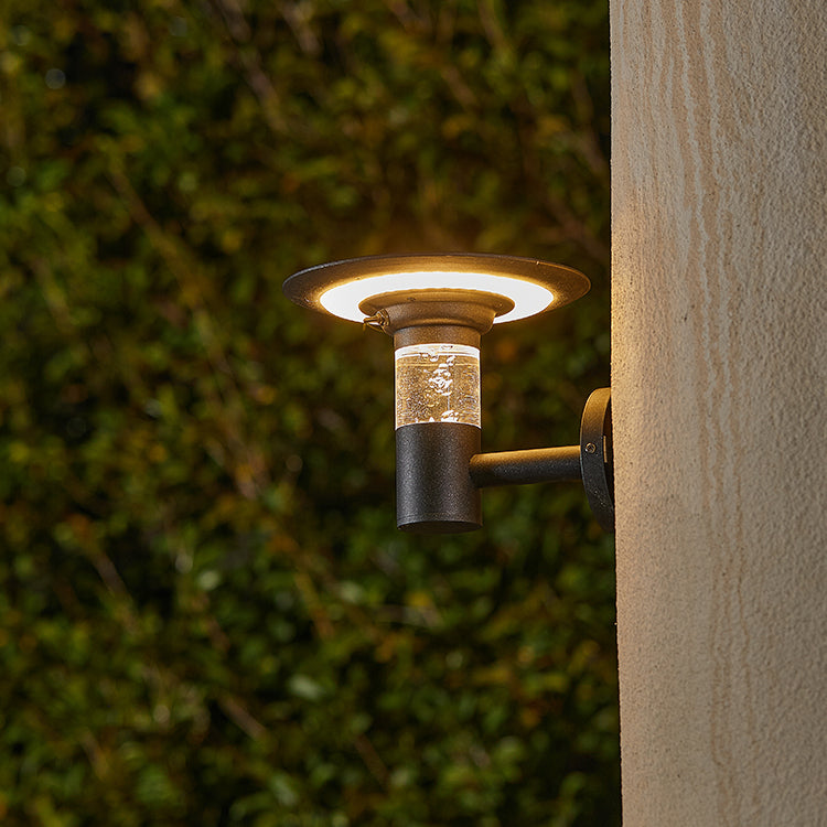 Outdoor wall light fixture on a building exterior with green foliage in the background