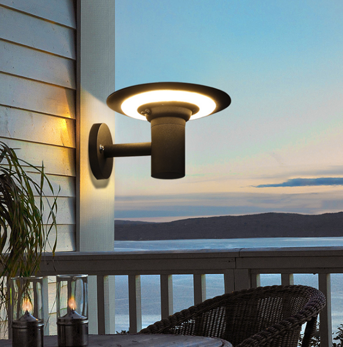 Outdoor wall light fixture on a deck with a scenic view of water and mountains.